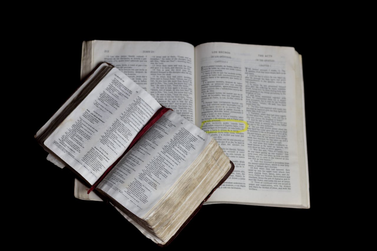 An open Bible on top of another against a plain black background.